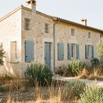 Maison provençale entourée de végétation débroussaillée, avec des volets métalliques fermés et de fines grilles sur les aérations, éclairée par une lumière estivale réaliste.