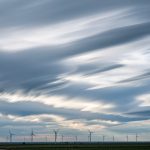 Paysage météorologique réaliste avec des nuages en mouvement, des lignes de vent et des éoliennes au loin, dans une ambiance pédagogique.