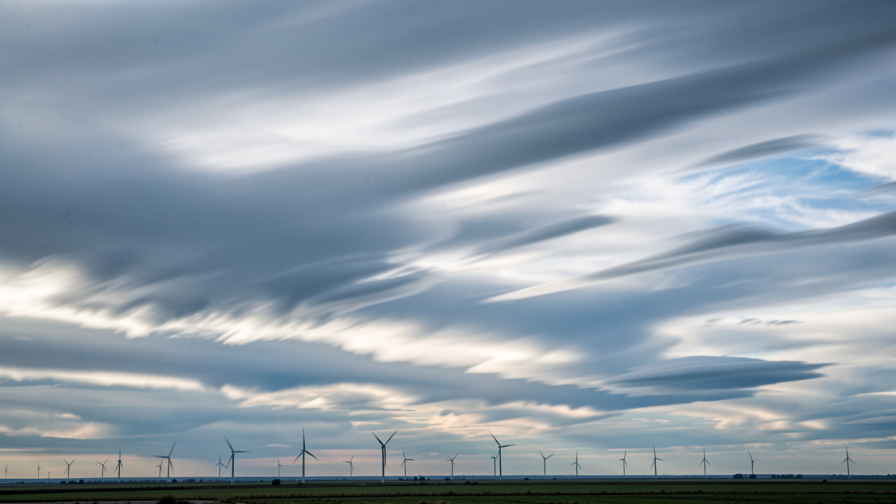 Paysage météorologique réaliste avec des nuages en mouvement, des lignes de vent et des éoliennes au loin, dans une ambiance pédagogique.